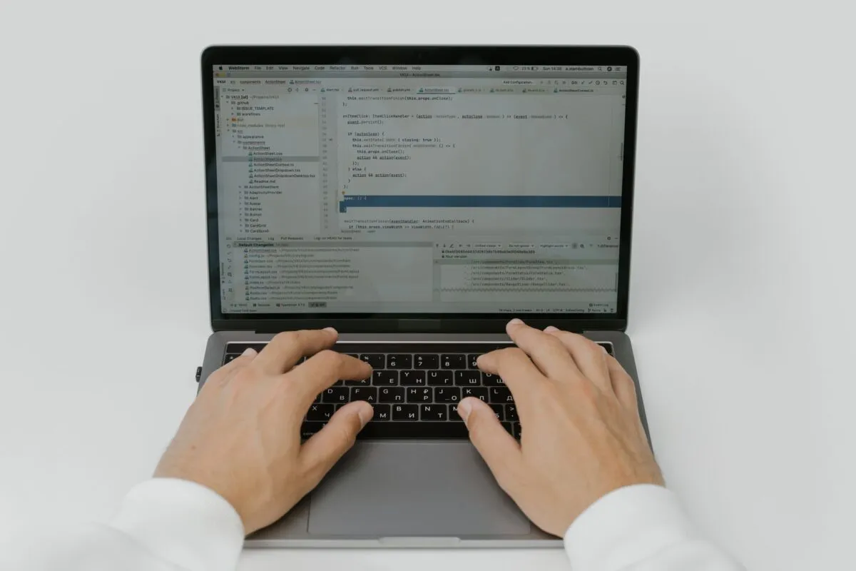 Pessoa digitando em um laptop com código aberto na tela.