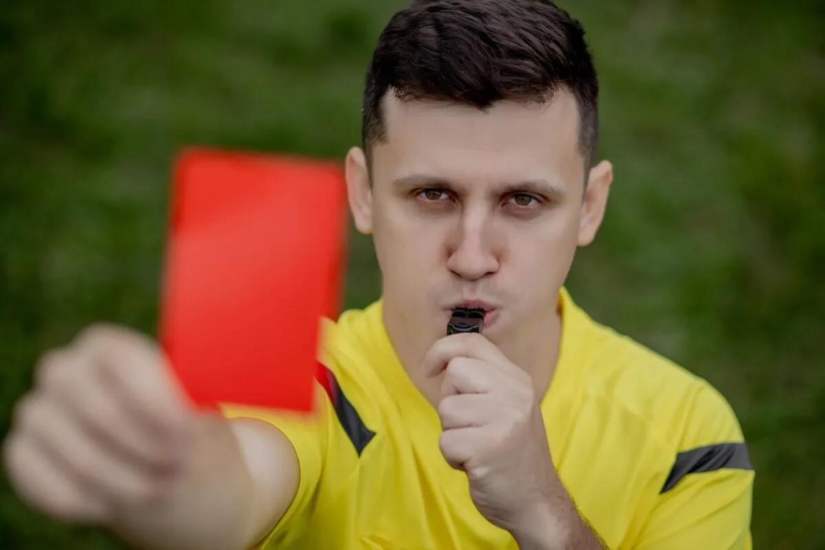 Árbitro em um uniforme amarelo levantando um cartão vermelho sob uma expressão séria