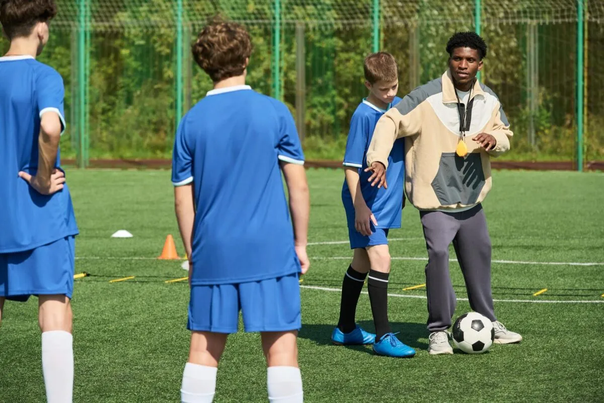 Um treinador demonstra técnicas de futebol a jovens atletas em um campo verde.